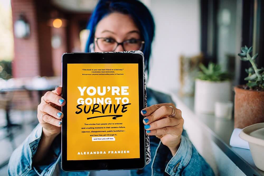 Photo of Alexandra holding a tablet device with e-book version of 'You're Going to Survive' in focus.