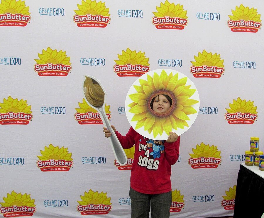Remy holding a sunflower prop with a hole punched for the face, and a spoon, for the SunButter photobooth; his shirt says "LIKE A BOSS"