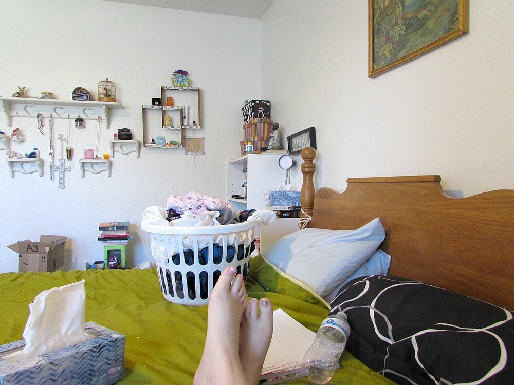 Photo of feet on bed, filled laundry basket behind feet; rest of room is out of focus