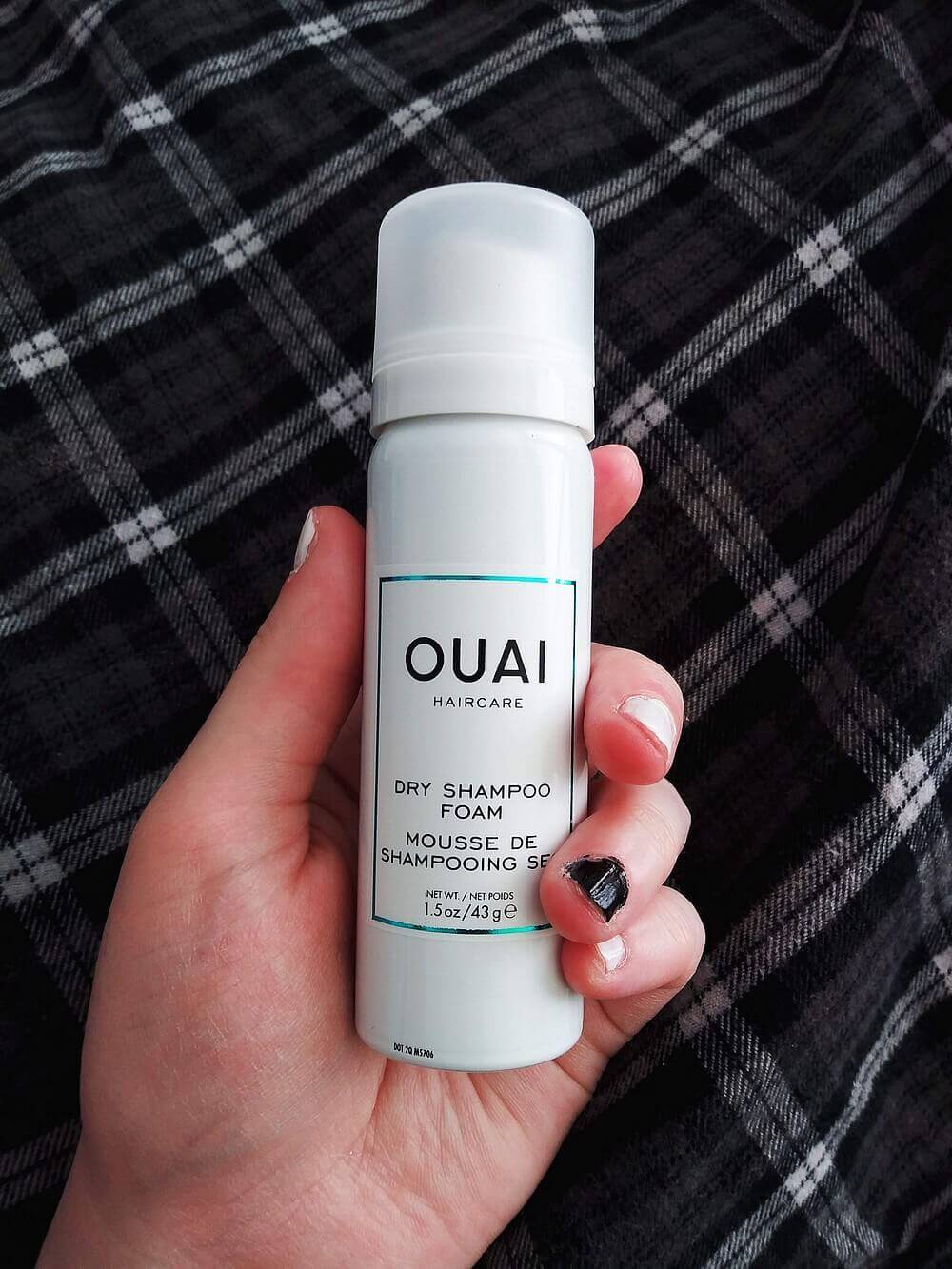 A canister of OUAI dry shampoo form in a hand; background is black-and-white Madras flannel top