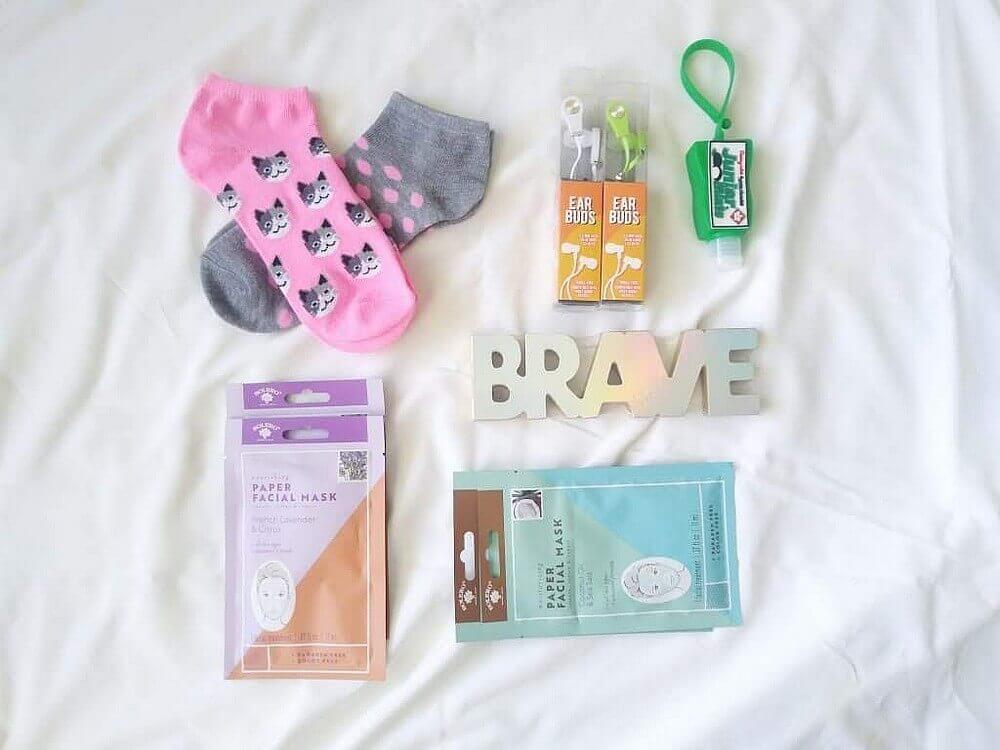 Two pairs of socks (pink & grey polka dots, and white/grey cats on pink); wooden "BRAVE" four paper facial masks; 2 pairs of ear bugs; Junior Mints®-scented hand sanitizer in a green holder