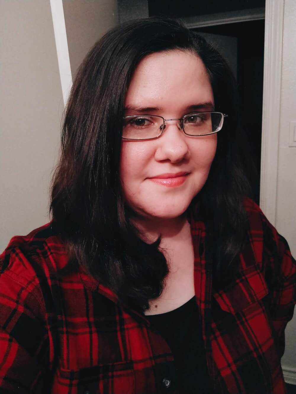 Selfie of me in glasses, a small smile, short hair, red plaid flannel