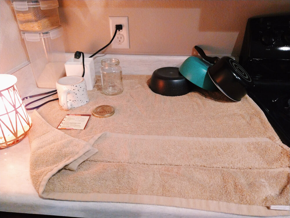 Mostly empty tan towel under clean dishes on top of corner counter