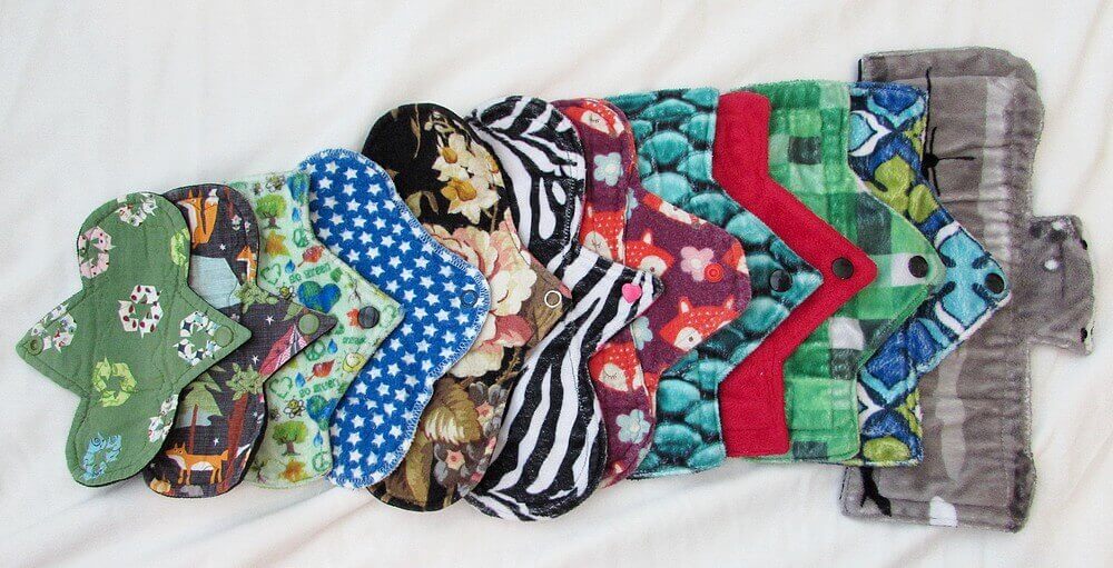 12 assorted cloth pads lay atop a white blanket in a line, slightly layered on the next