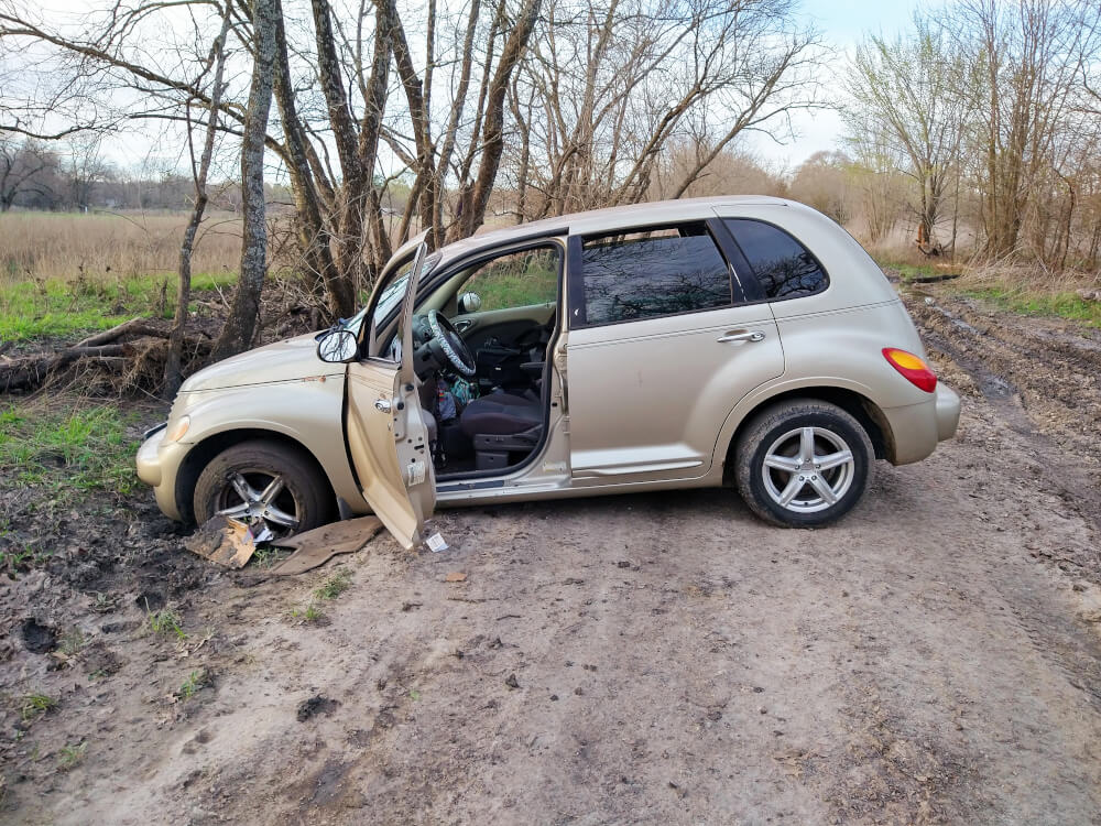 2005 PT Cruiser sideways on a dirt road, in front of some trees, stuck